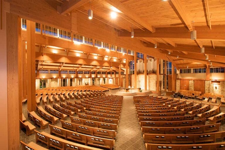 The Sancturary of Holy Family Catholic Church in Fond du Lac, Wisconsin illustrating the warm materials and color palette, clerestory windows, and pews arranged to maximize view of the raised Altar and Catholic Symbolism within the stained glass